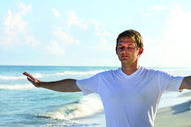 men meditating at the ocean with his arms spread and eyes closed