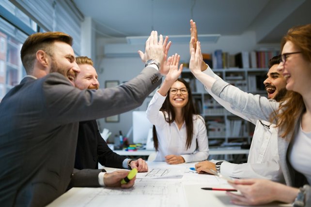 A business team smiling and giving a high five to celebrate their good work